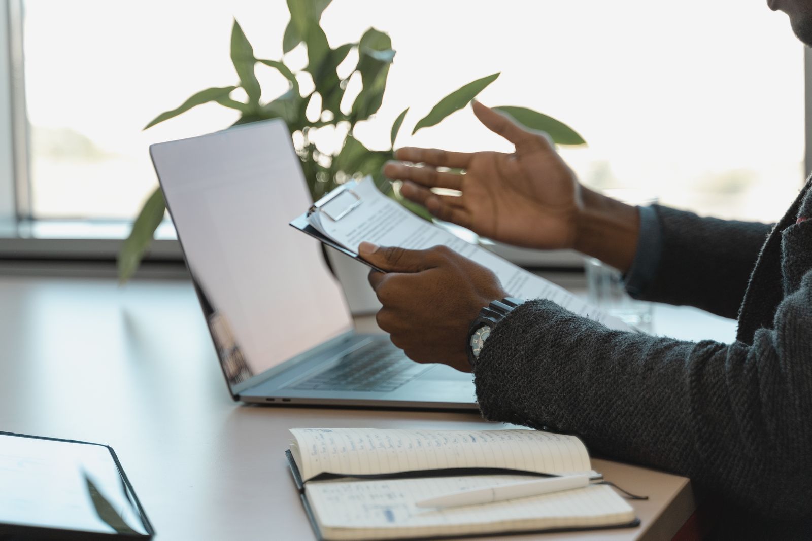 Hands reviewing documents beside a laptop and notebook